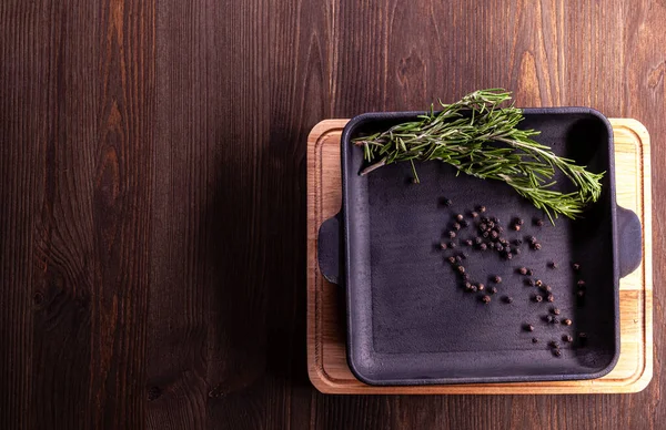 Biberiye, karabiber dökme demir tavaya yerleştirilmiş kesme tahtasıyla ahşap arkaplan ve metin için yer..