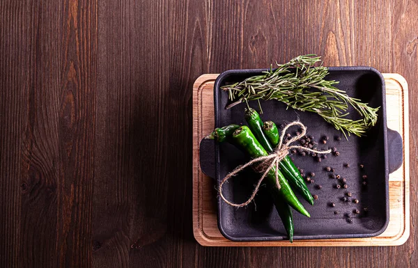 Biberiye, karabiber, yeşil biber dökme demir tavaya yerleştirilmiş kesme tahtası ve metin için yeri olan ahşap zemin..