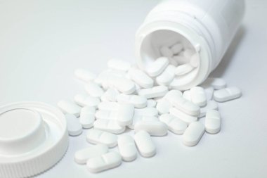 Beyaz konteynırdan dökülen haplar. Beyaz plastik ilaç şişesinden çıkan beyaz tıbbi haplar, beyaz arka plan. Seçici odak.