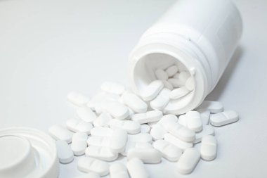 Beyaz konteynırdan dökülen haplar. Beyaz plastik ilaç şişesinden çıkan beyaz tıbbi haplar, beyaz arka plan. Seçici odak.