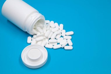 Beyaz konteynırdan dökülen haplar. Beyaz plastik ilaç şişesinden çıkan beyaz tıbbi haplar, beyaz arka plan. Seçici odak.