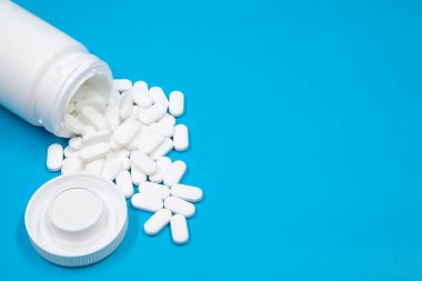Beyaz konteynırdan dökülen haplar. Beyaz plastik ilaç şişesinden çıkan beyaz tıbbi haplar, beyaz arka plan. Seçici odak.