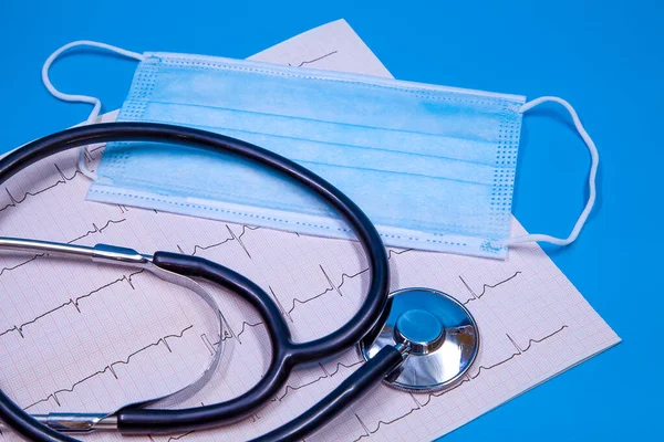 Stetoskop, cerrahi maske ve mavi arka planda ECG şerit konsepti.