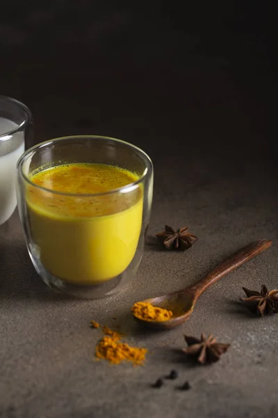 Golden milk with turmeric powder in glass over dark grunge background, copy space. Health and energy boosting, flu remedy, natural cold fighting drink. Clean eating, detox, weight loss concept