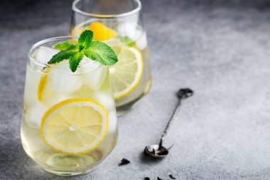 Limonlu, naneli ve buzlu soğuk yeşil çay, gri arka planda bardaklar, yaz içkileri, limonata.