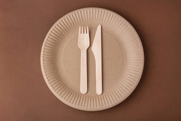 paper plate with a fork and knife, eco-friendly waste, on a brown background, disposable tableware, top view