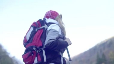 Kederli bir şekilde seyahat eden turist kız, macera arayışında, nehrin kenarında, ormanın içinden, dağın tepesine doğru yürüyor.