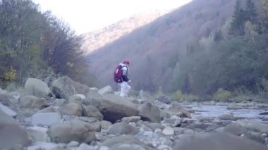 Kederli bir şekilde seyahat eden turist kız, macera arayışında, nehrin kenarında, ormanın içinden, dağın tepesine doğru yürüyor.