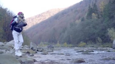 Kederli bir şekilde seyahat eden turist kız, macera arayışında, nehrin kenarında, ormanın içinden, dağın tepesine doğru yürüyor.