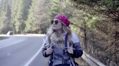 Kederli bir şekilde seyahat eden turist kız, macera arayışında, nehrin kenarında, ormanın içinden, dağın tepesine doğru yürüyor.