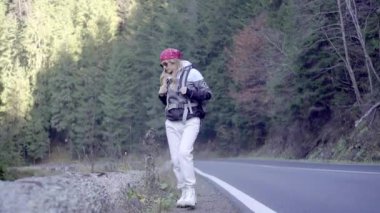 Kederli bir şekilde seyahat eden turist kız, macera arayışında, nehrin kenarında, ormanın içinden, dağın tepesine doğru yürüyor.