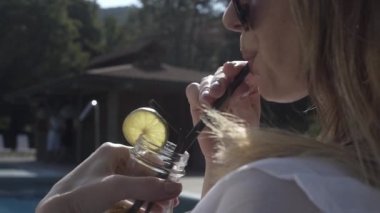 Kızlar havuz kenarında dinlenir, güneşlenir ve sohbet eder, kokteyl içerler.