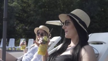 Kızlar havuz kenarında dinlenir, güneşlenir ve sohbet eder, kokteyl içerler.