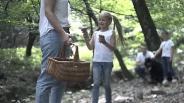 Ormanda Aile Yürüyüşü Macerası. Anne, baba ve kızlarının mutlu aileleri kozalaklı ormanda el ele yürüyorlar. Ebeveynler çocuklara güzel ağaçlar gösteriyor. Çocuklar mantar toplar.