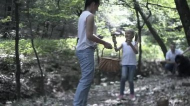 Ormanda Aile Yürüyüşü Macerası. Anne, baba ve kızlarının mutlu aileleri kozalaklı ormanda el ele yürüyorlar. Ebeveynler çocuklara güzel ağaçlar gösteriyor. Çocuklar mantar toplar.