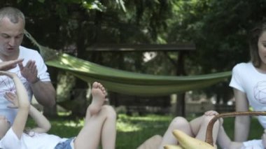 Mutlu aileler dışarıda çayırda piknik yapıyorlar. Ebeveynler ve çocuklar hafta sonları halk parkında eğleniyorlar. Pozitif ruh hali, ebeveynlik, çocukluk..