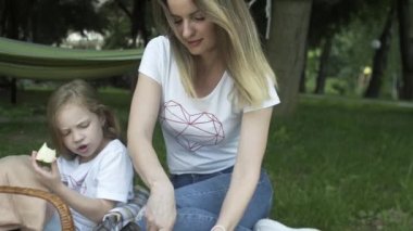 Mutlu aileler dışarıda çayırda piknik yapıyorlar. Ebeveynler ve çocuklar hafta sonları halk parkında eğleniyorlar. Pozitif ruh hali, ebeveynlik, çocukluk..