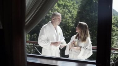 Karı koca tatilde dağlarda balkonda kahve içiyorlar.