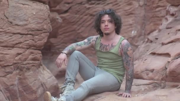 男は峡谷に座ってカメラのポーズをとって旅熱サハラ — ストック動画