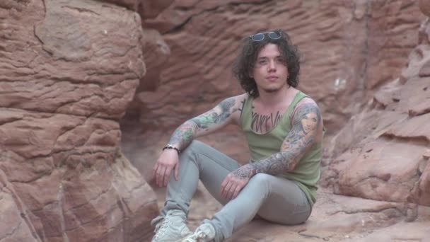 男は峡谷に座ってカメラのポーズをとって旅熱サハラ — ストック動画