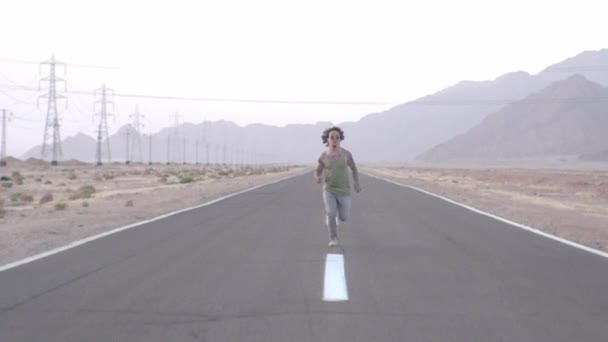 那家伙在沙漠的高速公路上奔跑 慢动作的人沿路沿着斑驳的条带跑 慢动作的样子 全神贯注地跑过沙漠 留着卷发的英俊男子跑得非常漂亮 — 图库视频影像
