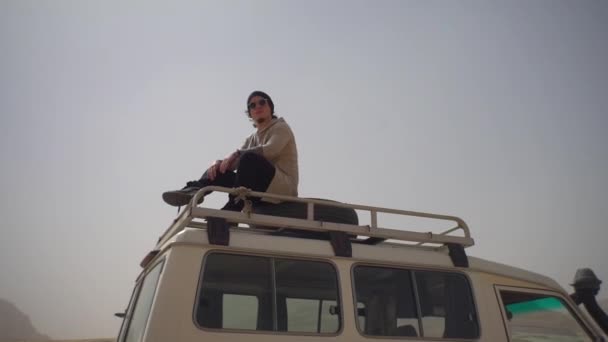 車の屋根の上の男は砂漠を旅する — ストック動画