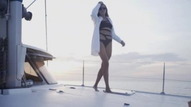 Seksi kız gün batımında Tayland 'da adanın yakınında yelken açan bir yatta dans ediyor.