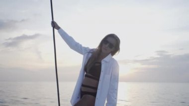 Seksi kız gün batımında Tayland 'da adanın yakınında yelken açan bir yatta dans ediyor.