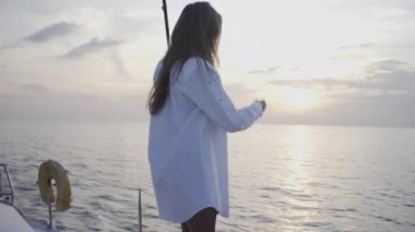 Seksi kız gün batımında Tayland 'da adanın yakınında yelken açan bir yatta dans ediyor.