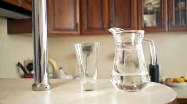 Su bir sürahide mutfaktaki bir bardağa dökülüyor.