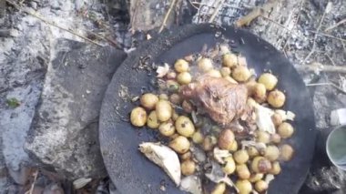 Gölün kenarında bir balıkçı, ateşte patates pişiriyor, tarla koşulları, ormanda yaşıyor, ateşte yiyor, doğada yaşıyor.