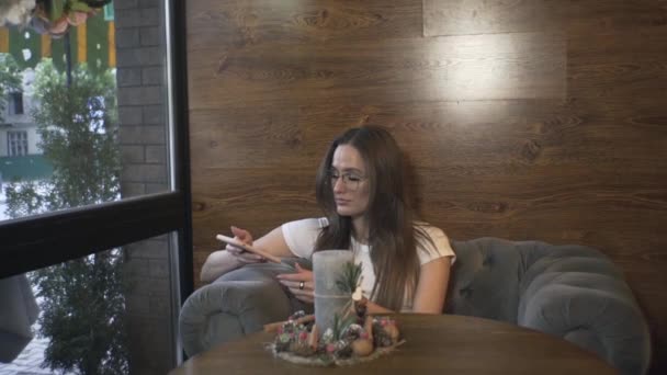Девушка Сидит Столом Кафе Ресторане Ждет Кого Смотрит Телефон Симпатичная — стоковое видео