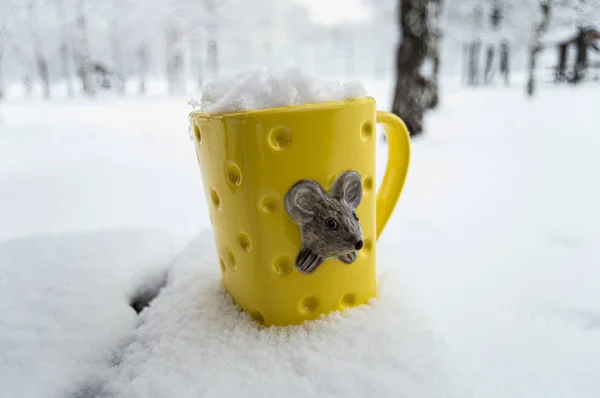 Yellow mug with a rat full of snow in the winter forest with bokeh.