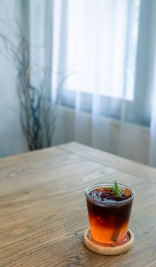 Bir bardak buzlu siyah çay ve biberiyeyle süslenmiş ahşap bir masa üzerinde fotokopi alanı en üstte dikey formatta pencere ışığı arka planda.