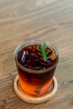 Bir bardak buzlu siyah çay. Biberiyeyle süslenmiş, ahşap bir masada. Üzerinde dikey olarak fotokopi alanı var.