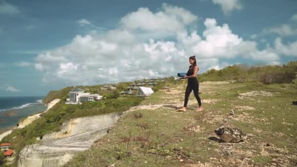 Femme mince mettant tapis de yoga sur le bord de la falaise — Video