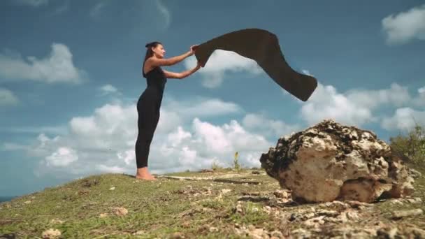 Mulher magro colocando tapete de ioga na borda do penhasco — Vídeo de Stock