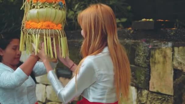 Touristin hilft Balinesin, Vase mit Opfergaben auf den Kopf zu stellen — Stockvideo