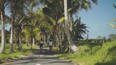 İki kadın palmiye ağaçları arasında bisiklet sürme