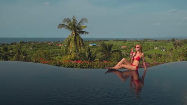 Junge Frau im roten Bikini trinkt Saft am Rande des Infinity-Pools, Meerblick — Stockvideo