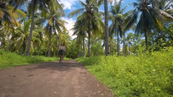 Fille promenades à vélo entre les palmiers luxuriants sur une journée ensoleillée — Video