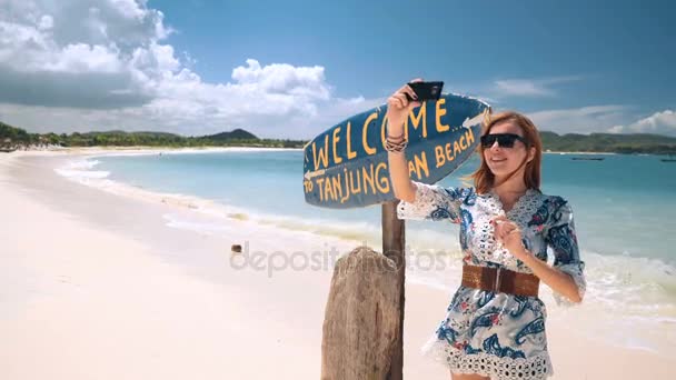 Mädchen macht Selfie in der Nähe von Tanjung aan weißen Sandstrand Schild in Lombok, Indonesien — Stockvideo