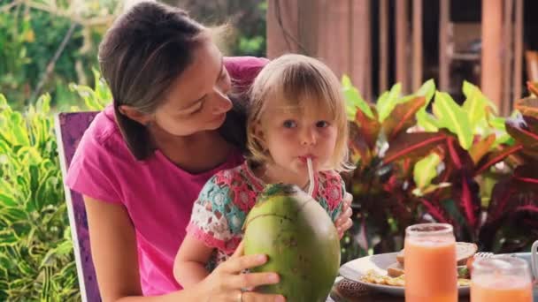 Madre ayuda a su pequeña hija a beber jugo de coco — Vídeo de stock