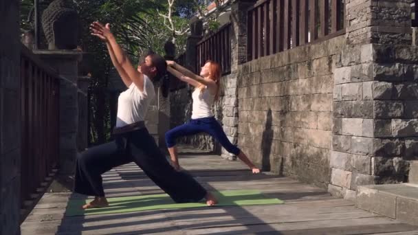 Dos mujeres haciendo yoga guerrero posan en Ubud, Bali — Vídeos de Stock