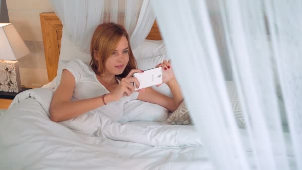 Dívka pomocí smartphone v postel s nebesy — Stock video