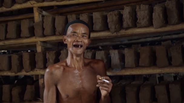 Vieil homme indonésien fumant dans une usine de tuiles — Video
