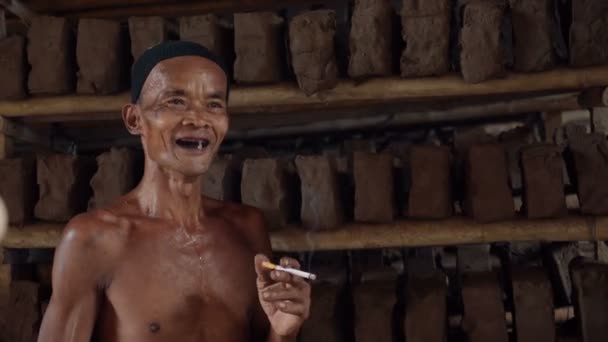 Viejo hombre indonesio fumando en fábrica de azulejos — Vídeo de stock