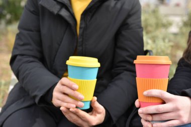 two girls sitting outdoors holding coffee cup .Sustainable lifestyle 