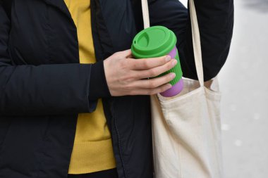 Yeniden kullanılabilir kahve fincanını tutan kadın eller açık havada bir çantaya koyuyor. Sıfır kayıp. Sürdürülebilir yaşam tarzı kavramı.