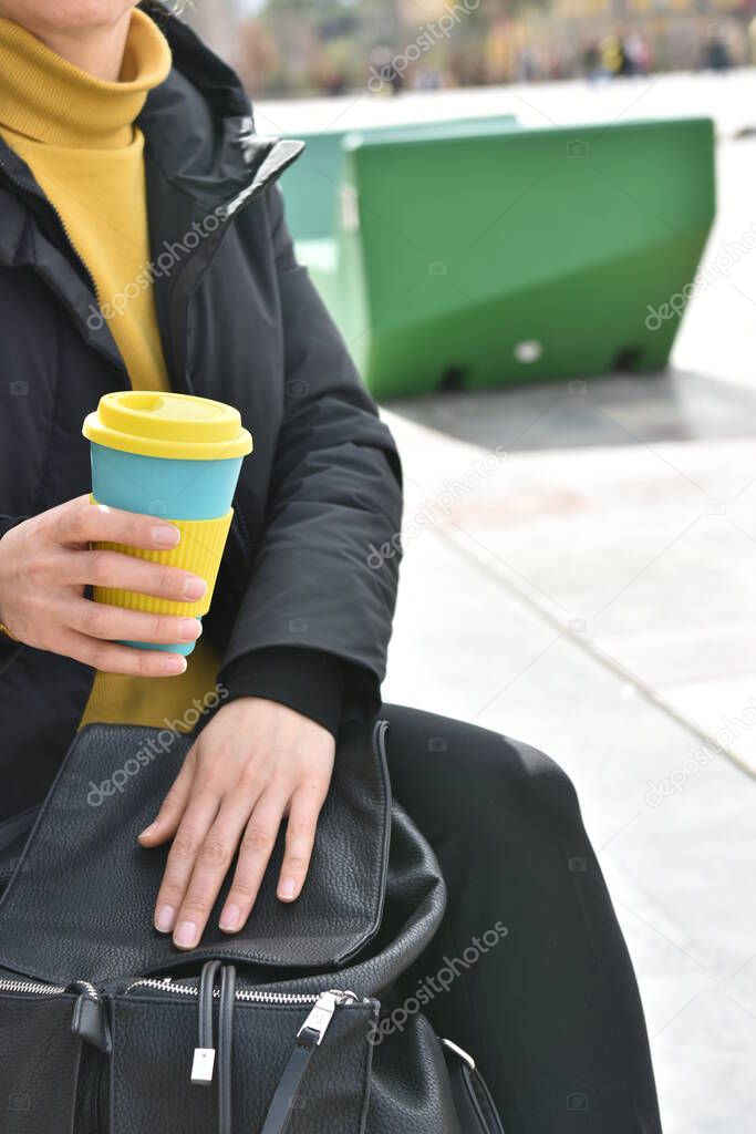Female hands holding reusable coffee cup putting into a bag outdoors. Zero waste. Sustainable lifestyle concept.
